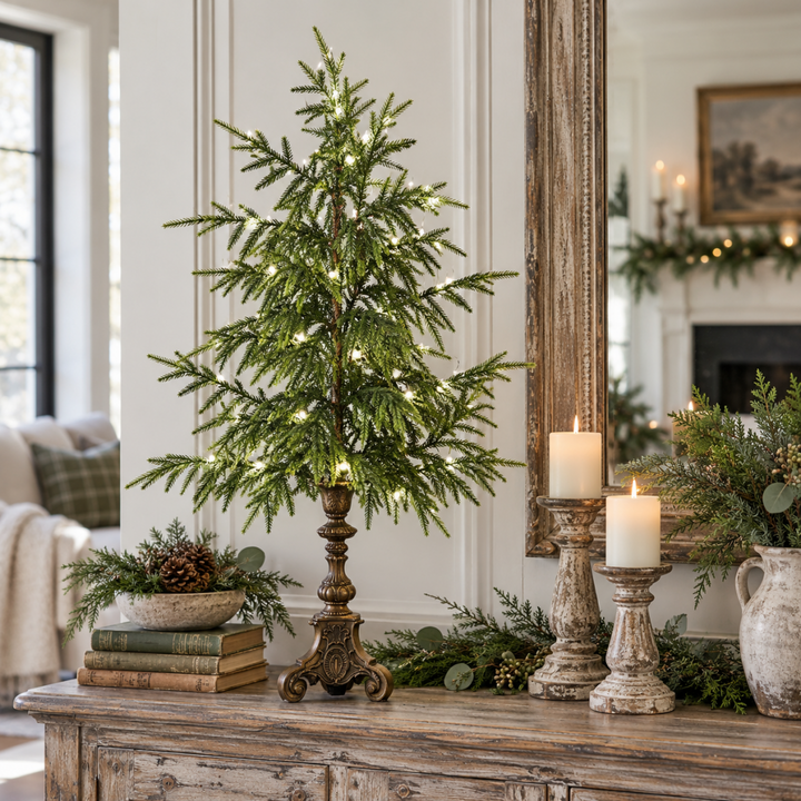 Large lighted Norfolk pine tree on a wooden console with books