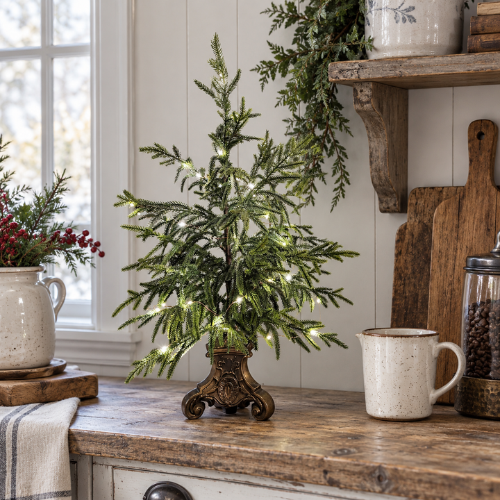 Small lighted Norfolk pine tree on a kitchen counter beside a mug